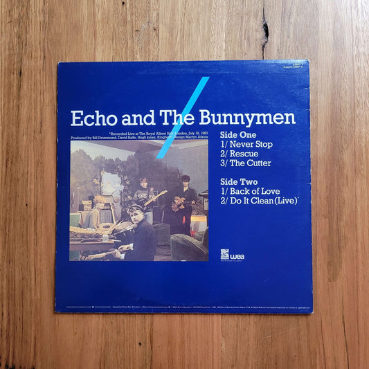 A blue vinyl record sleeve for Echo and The Bunnymen, featuring a tracklist on the right and a small album photo on the left, placed on a wooden surface.