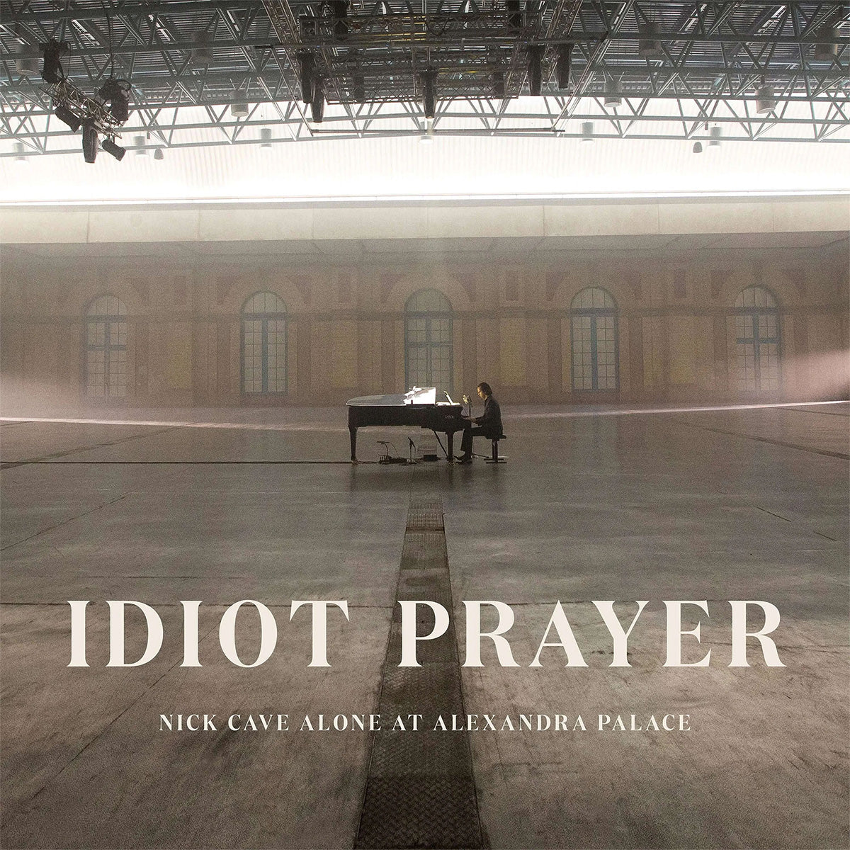 Album cover for 'Idiot Prayer' by Nick Cave, showing a person at a piano in a large hall.