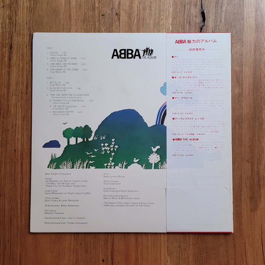 ABBA's 'A Love Like This' 12-inch vinyl record sleeve, featuring a white cover with Japanese text, track listings, and a colorful graphic of a green hill and blue mountains, laid flat on a wooden surface.