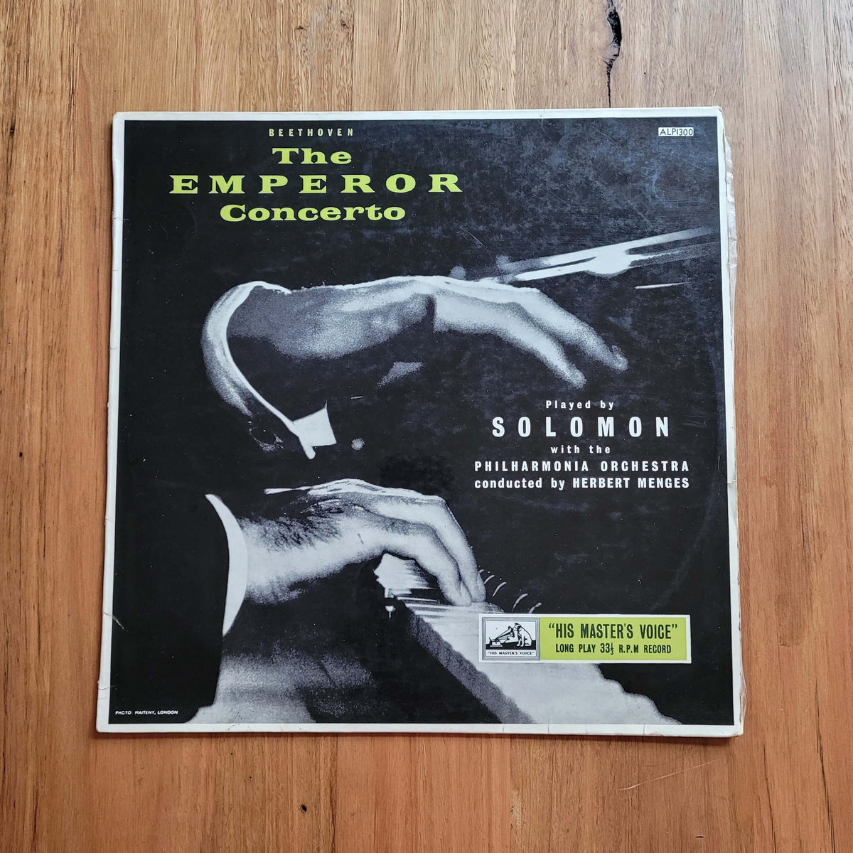 A vinyl record sleeve for 'The Emperor Concerto' with Solomon, photographed flat on a wooden tabletop. The cover is mostly black and white with yellow-green title text and a small yellow label at the bottom.