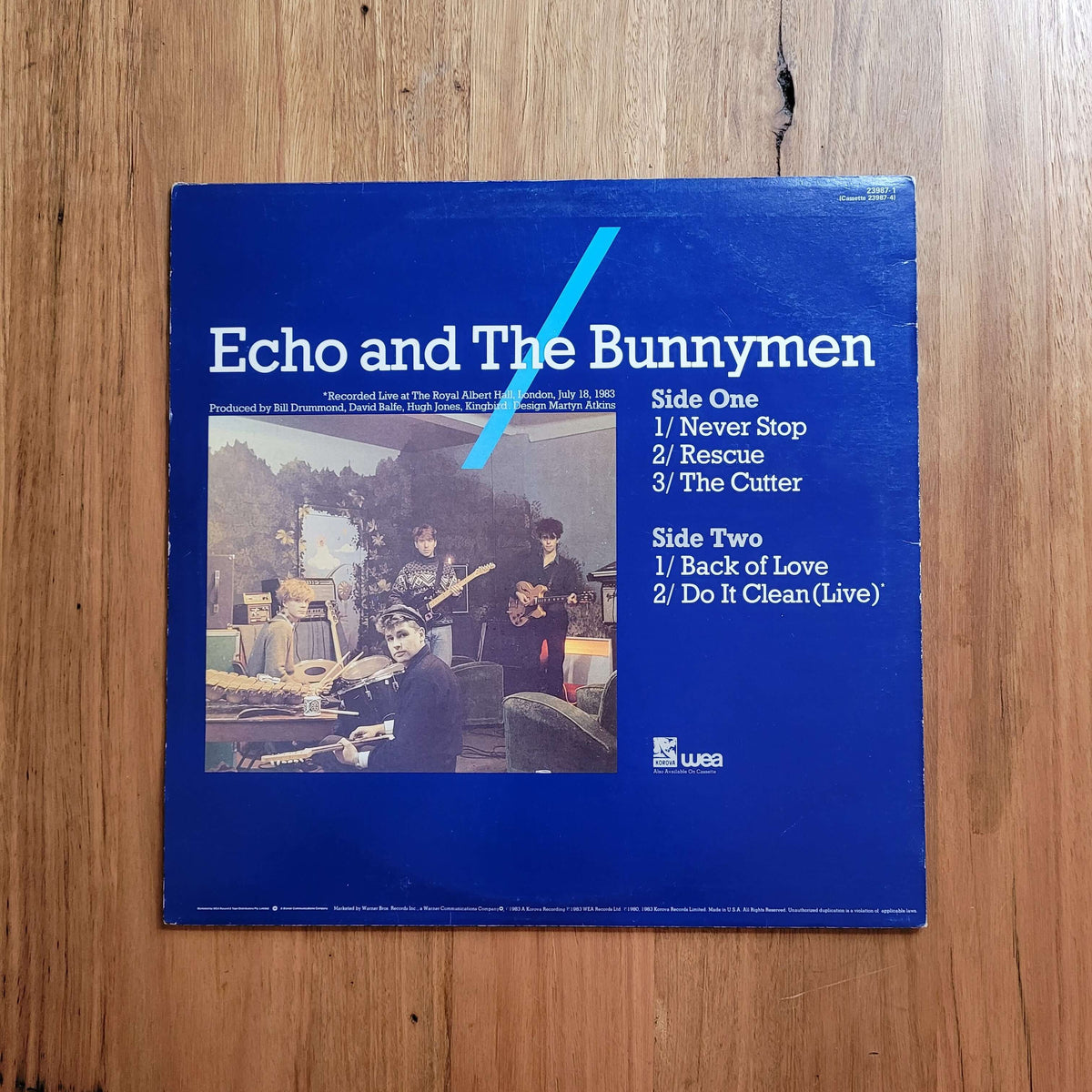 A blue vinyl record sleeve for Echo and The Bunnymen, featuring a tracklist on the right and a small album photo on the left, placed on a wooden surface.