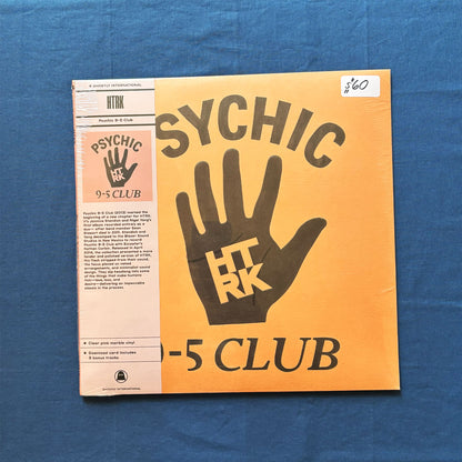 A vinyl record sleeve for HTK's 'Psychic 9-5 Club' lies on a textured blue fabric background. The cover features a yellow-to-orange gradient background with a large dark brown hand graphic containing the letters 'HTK' and 'RK', and the words 'PSYCHIC 9-5 CLUB' in bold.