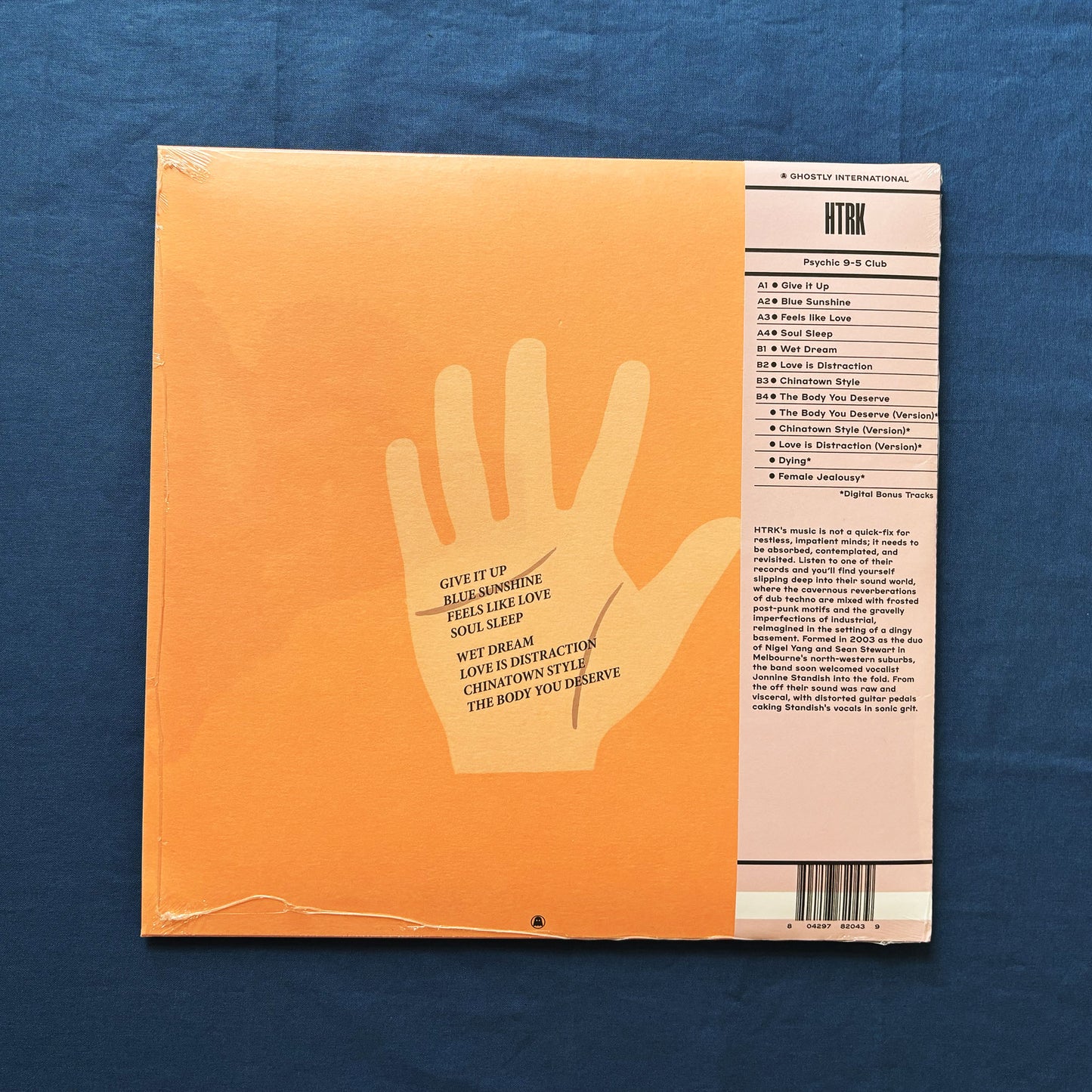 Back of vinyl record cover for HTRK's Psychic 9-5 cLUB with a hand line and text on an orange background