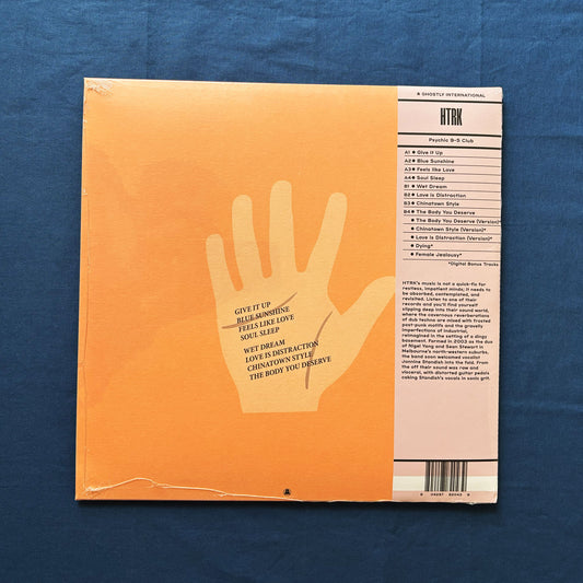 Back of vinyl record cover for HTRK's Psychic 9-5 cLUB with a hand line and text on an orange background