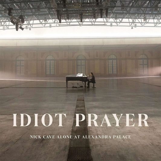 Album cover for 'Idiot Prayer' by Nick Cave, showing a person at a piano in a large hall.