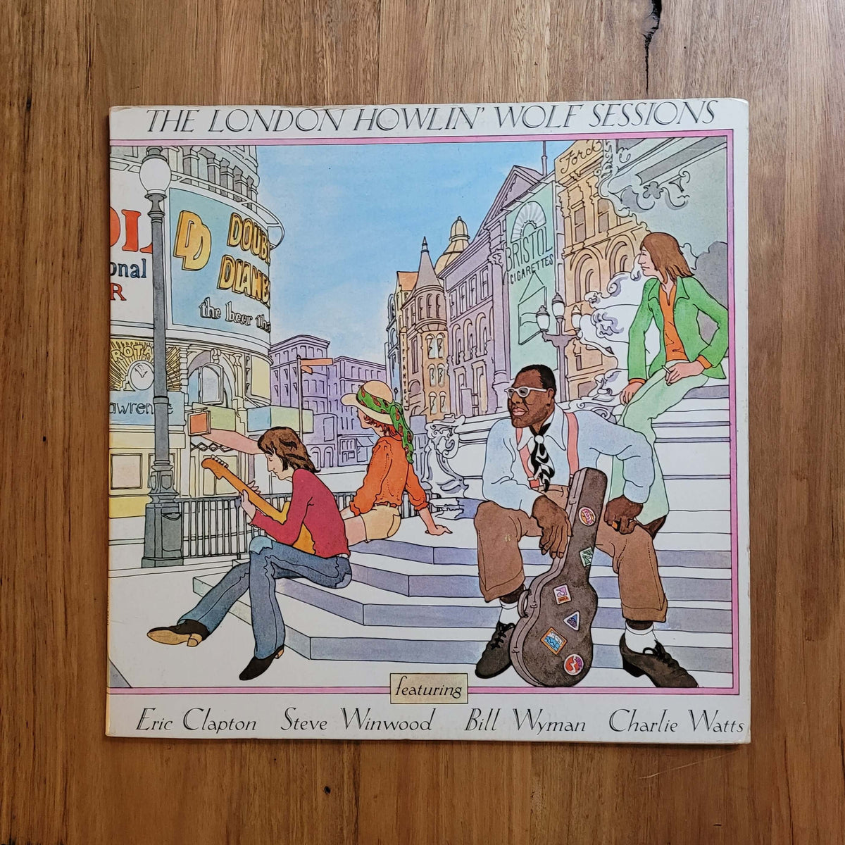 The London Howlin' Wolf Sessions vinyl record album cover by Eric Clapton, Steve Warneke, Bill Wyman, and Charlie Watts, displayed flat on a wooden floor.