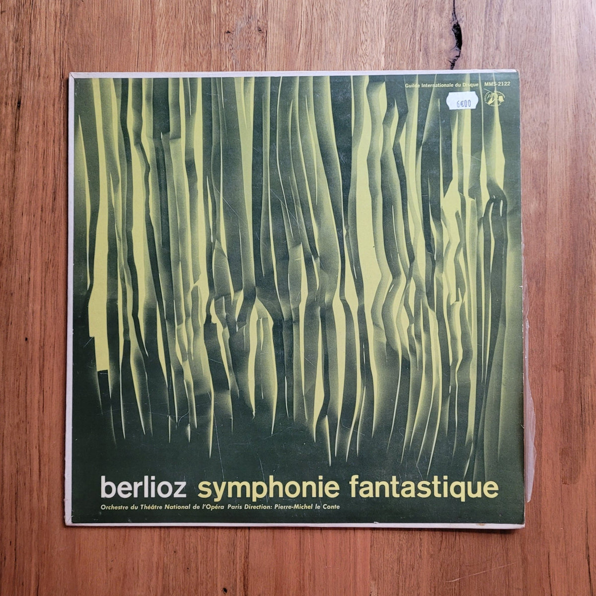 A vinyl record sleeve for Berlioz's 'Symphonie fantastique' lies on a wooden tabletop. The sleeve features an abstract green and yellow striped design with the title in white text at the bottom.