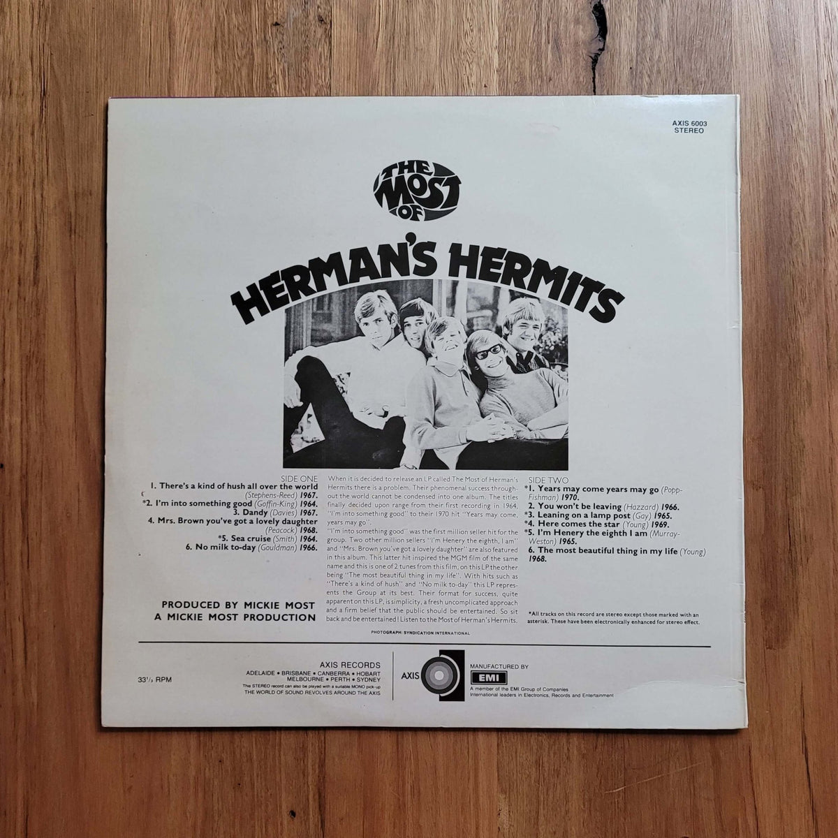 The back cover of a Herman's Hermits 12-inch vinyl record, featuring the band members in a black-and-white photo and track listings, placed on a wooden floor.