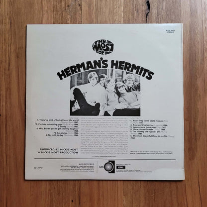 The back cover of a Herman's Hermits 12-inch vinyl record, featuring the band members in a black-and-white photo and track listings, placed on a wooden floor.