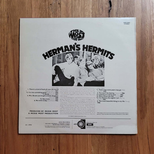 The back cover of a Herman's Hermits 12-inch vinyl record, featuring the band members in a black-and-white photo and track listings, placed on a wooden floor.
