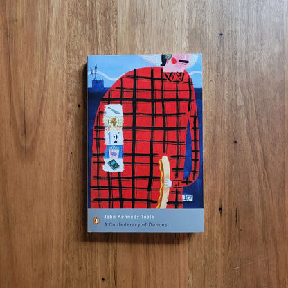 Cover of John Kennedy Toole - A Confederacy of Dunces (Paperback) on wooden background, showcasing artwork.