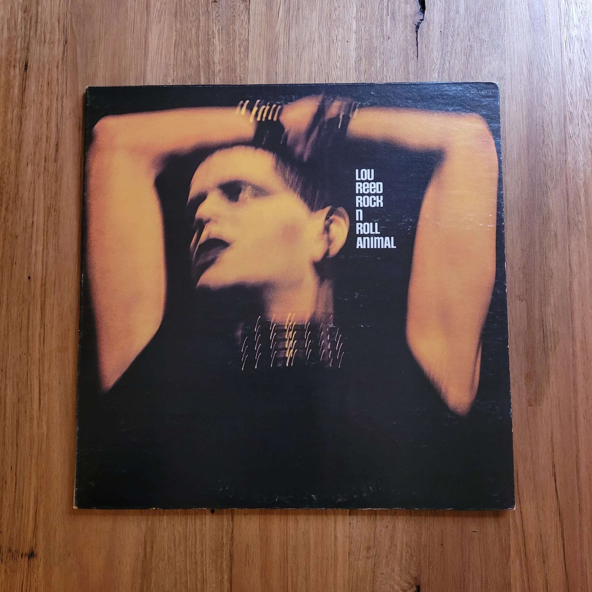 A vinyl record sleeve for Lou Reed's 'A Room with a View' resting on a wooden tabletop. The cover features a dramatic portrait of Lou Reed with his arms behind his head against a dark background, with the text 'LOU REED ROCK N' ROLL ANIMAL' printed on the right.